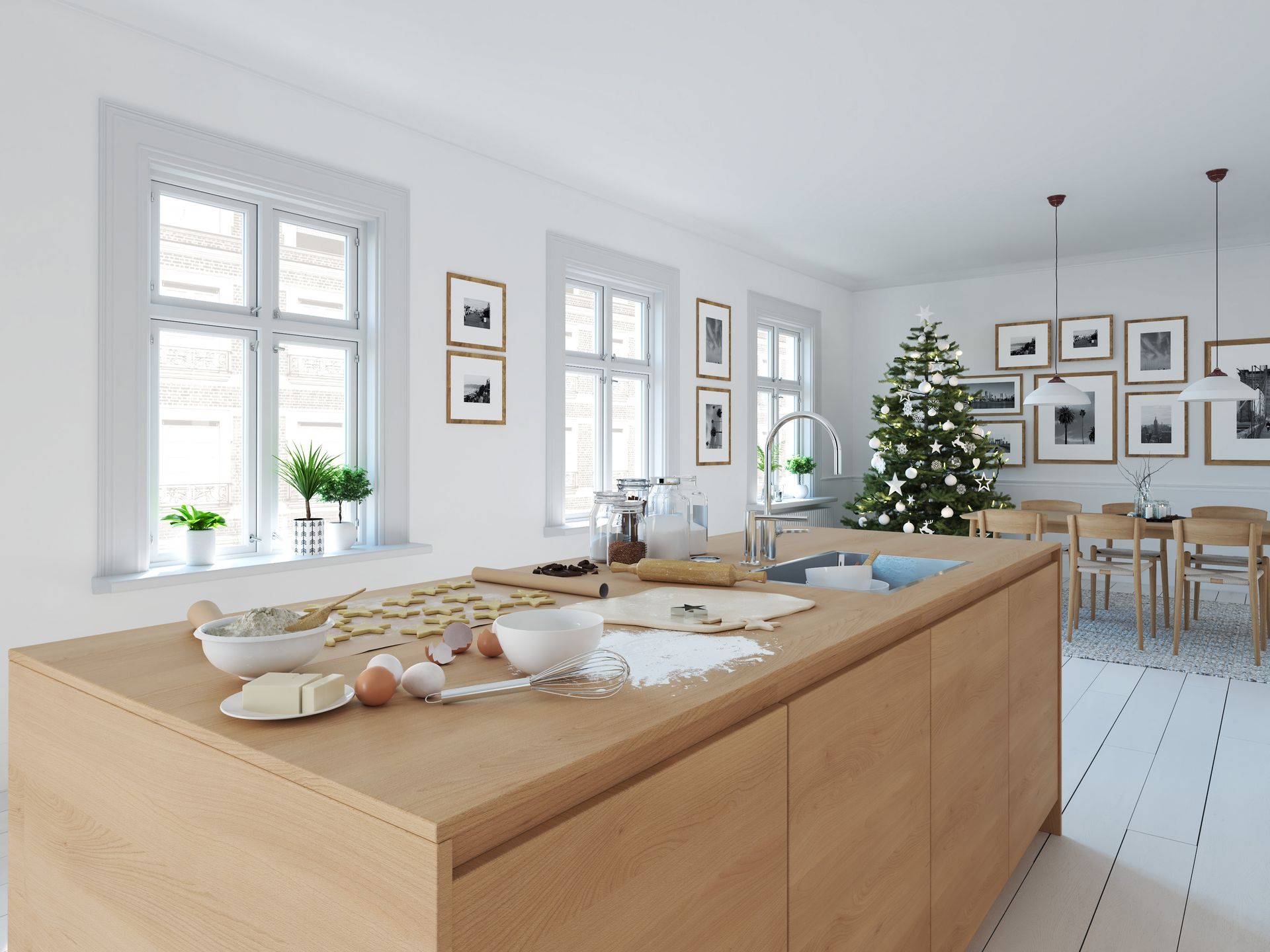 Light-filled kitchen with wooden island, ingredients for baking, Christmas tree in the background, and windows overlooking a bright outdoor view.