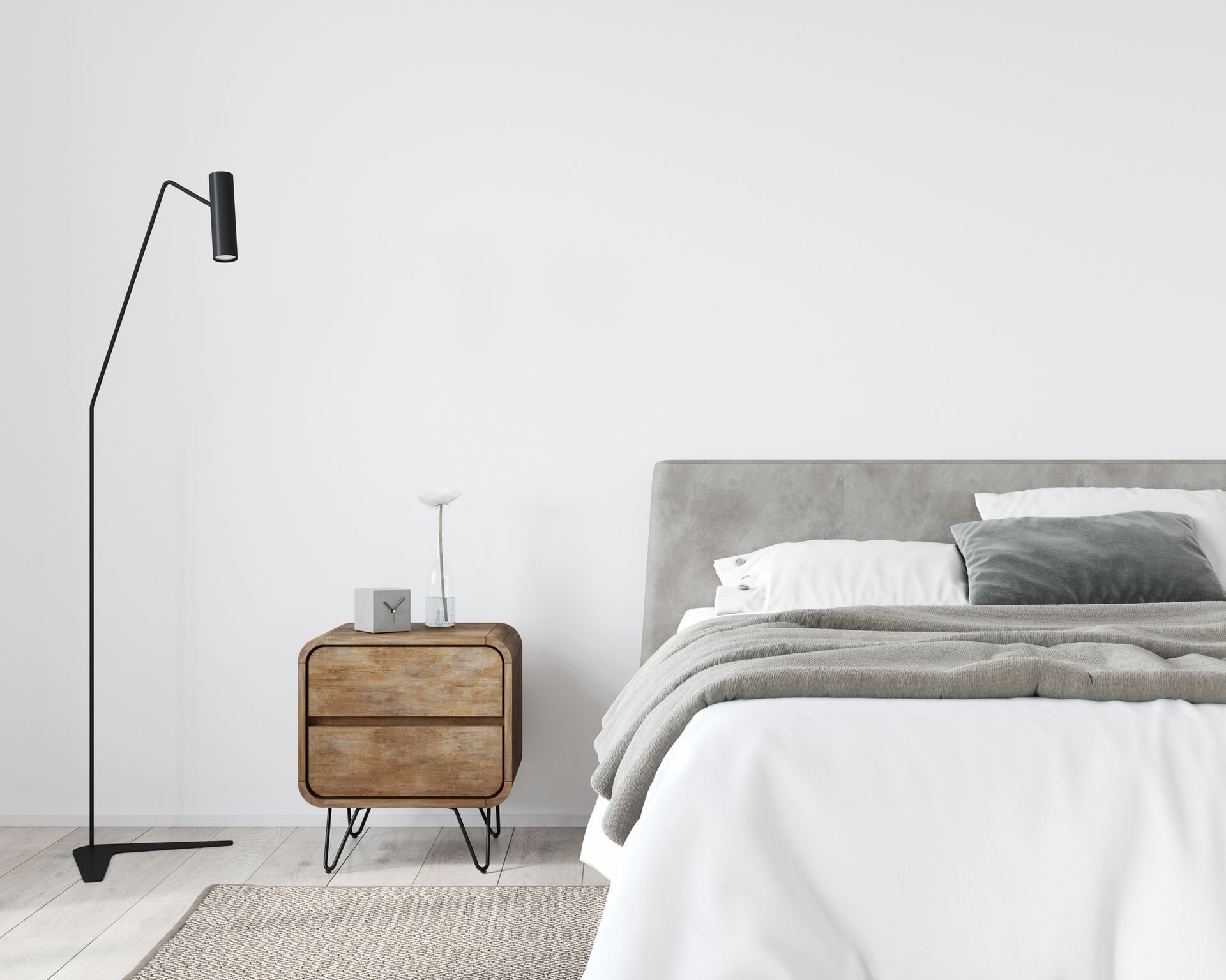 Bedroom interior with a bed, nightstand, floor lamp, and rug against a white wall. The bed has a grey headboard and a blanket.