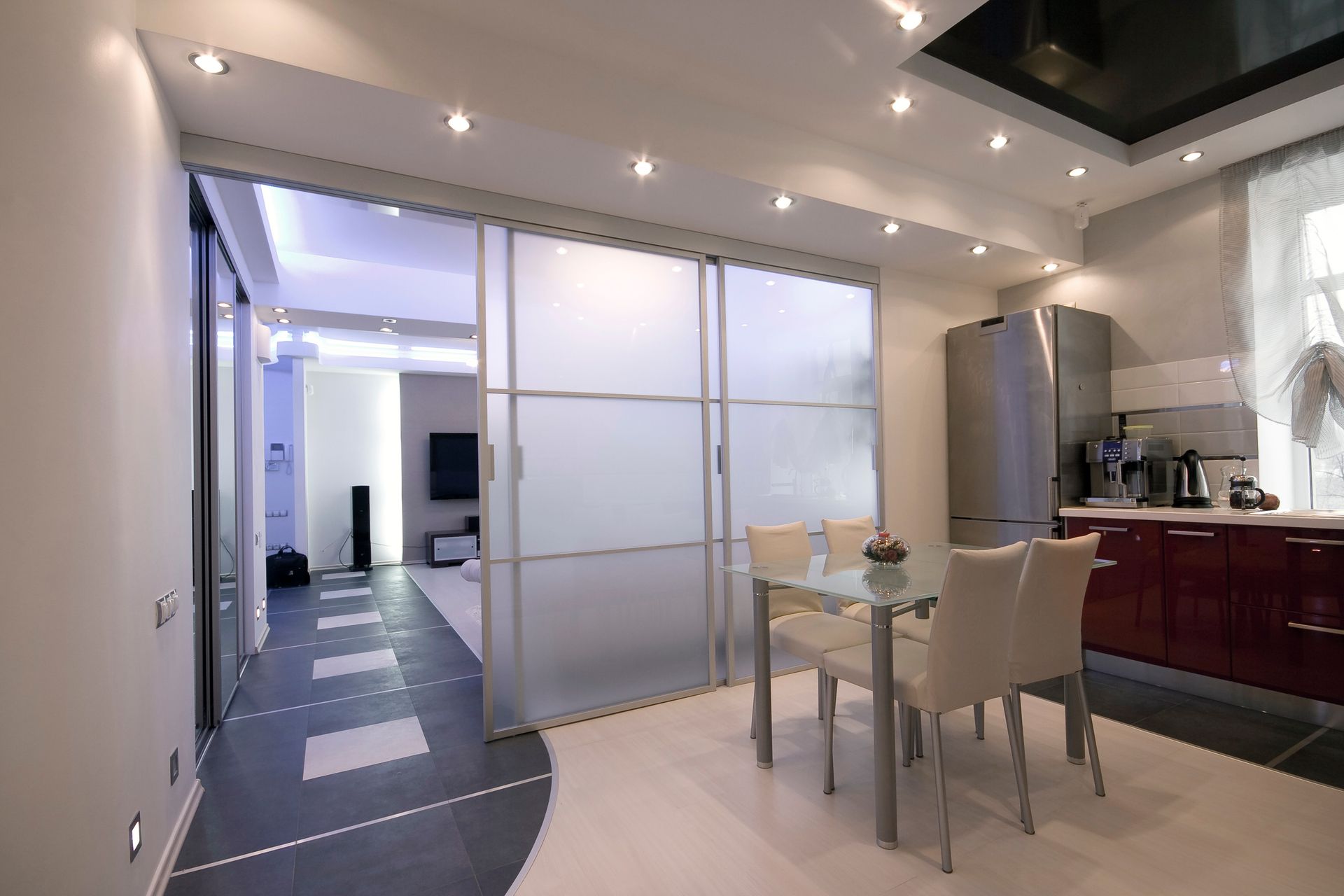 Modern apartment interior featuring a kitchen with red cabinets, dining area, and a living room separated by frosted sliding doors.