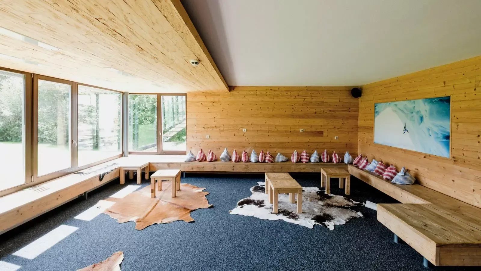 Gemütliche Lounge mit Holzvertäfelung, großen Fenstern und Sitzbänken mit Kissen. Tierfellteppiche auf dem Boden.