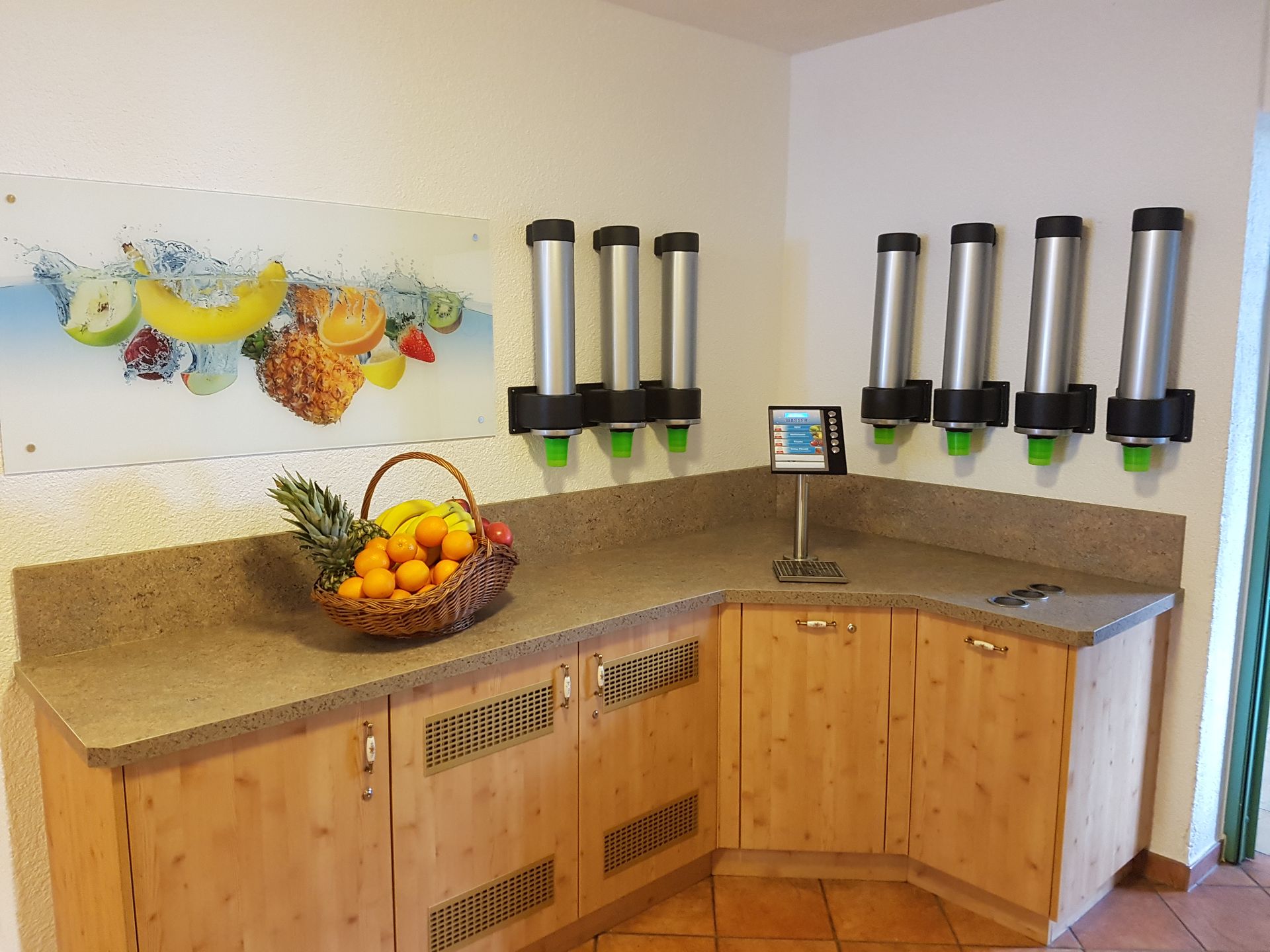 In einer Küchenecke stehen Fruchtsaftspender. Auf der Arbeitsfläche unter den Spendern steht ein Obstkorb.