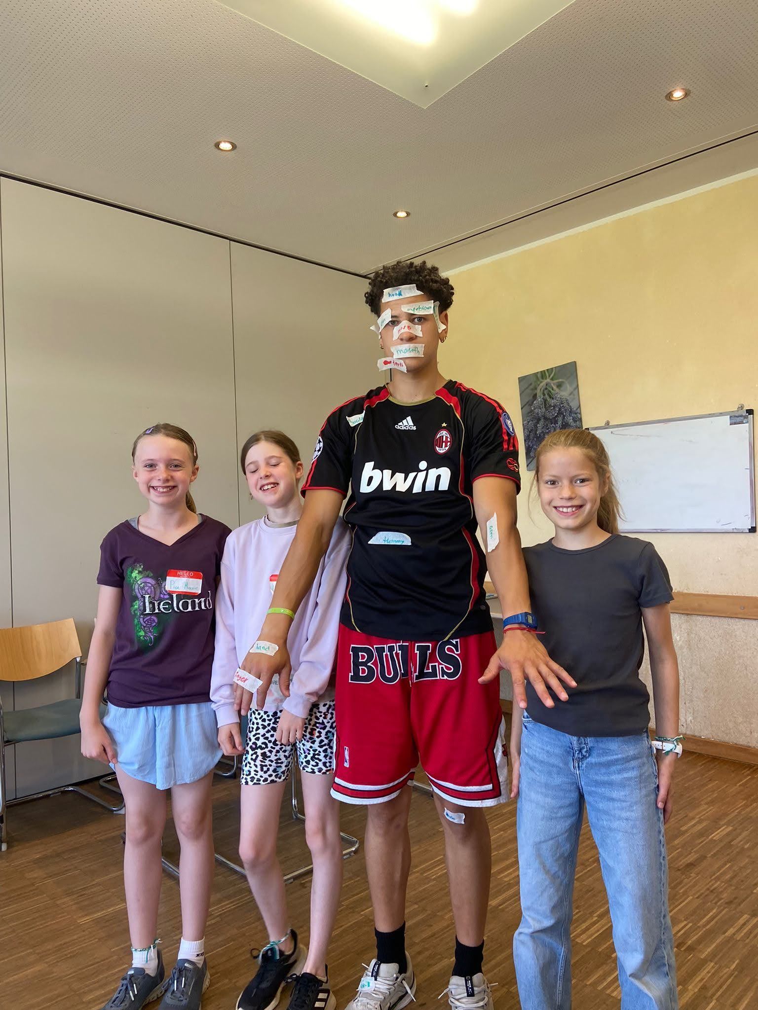 Vier Personen stehen in einem Innenraum; eine große Person trägt Sensoren im Gesicht und am Arm.