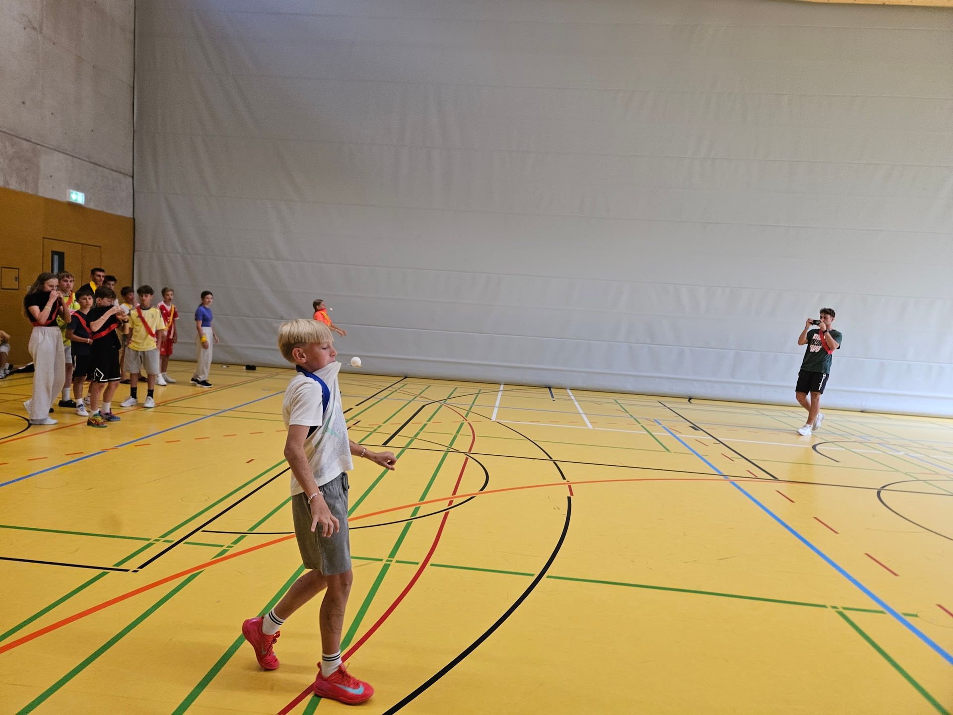 Ein Junge wirft einen Ball in einer Turnhalle, andere Leute schauen zu.