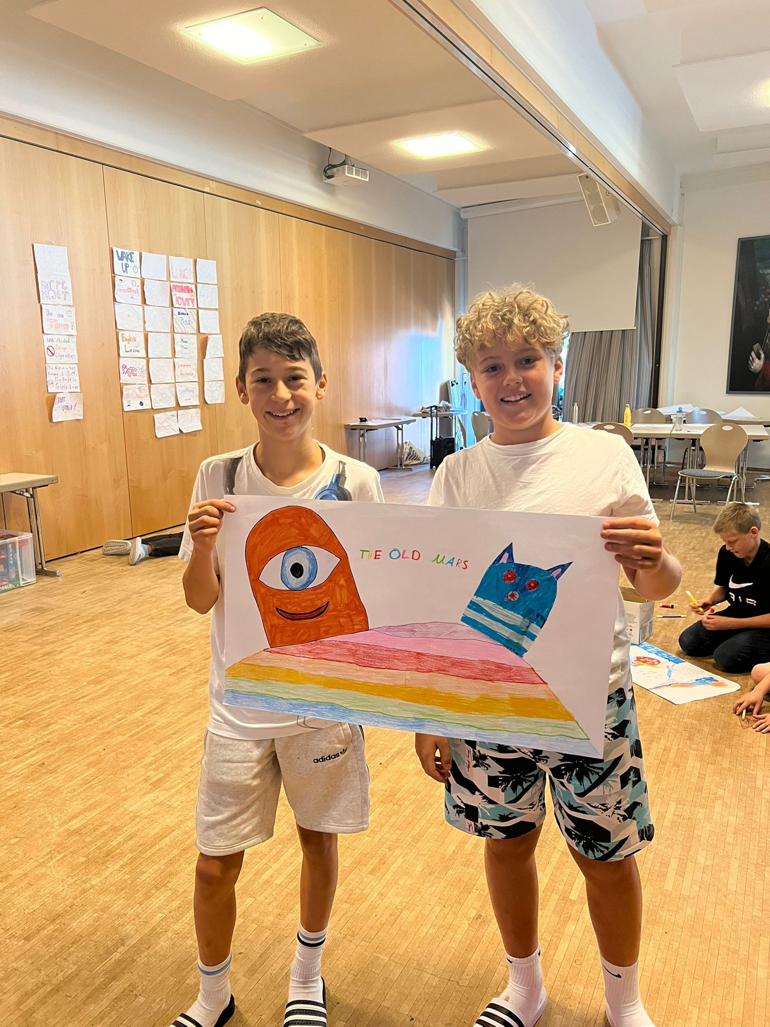 Zwei Jungen halten in ihrem Zimmer bunte Zeichnungen von Comicmonstern und einem Regenbogen in den Händen.