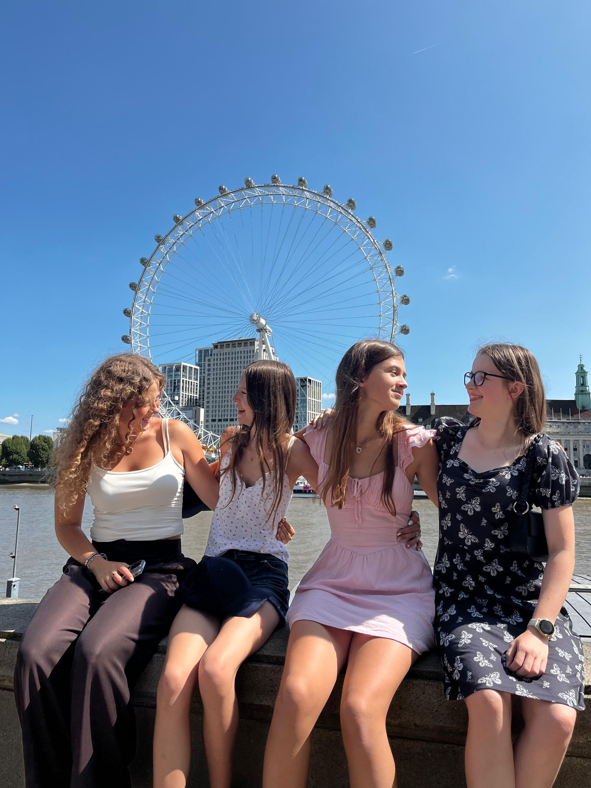 Vier Menschen lächeln und umarmen sich vor dem London Eye. Es ist ein sonniger Tag.