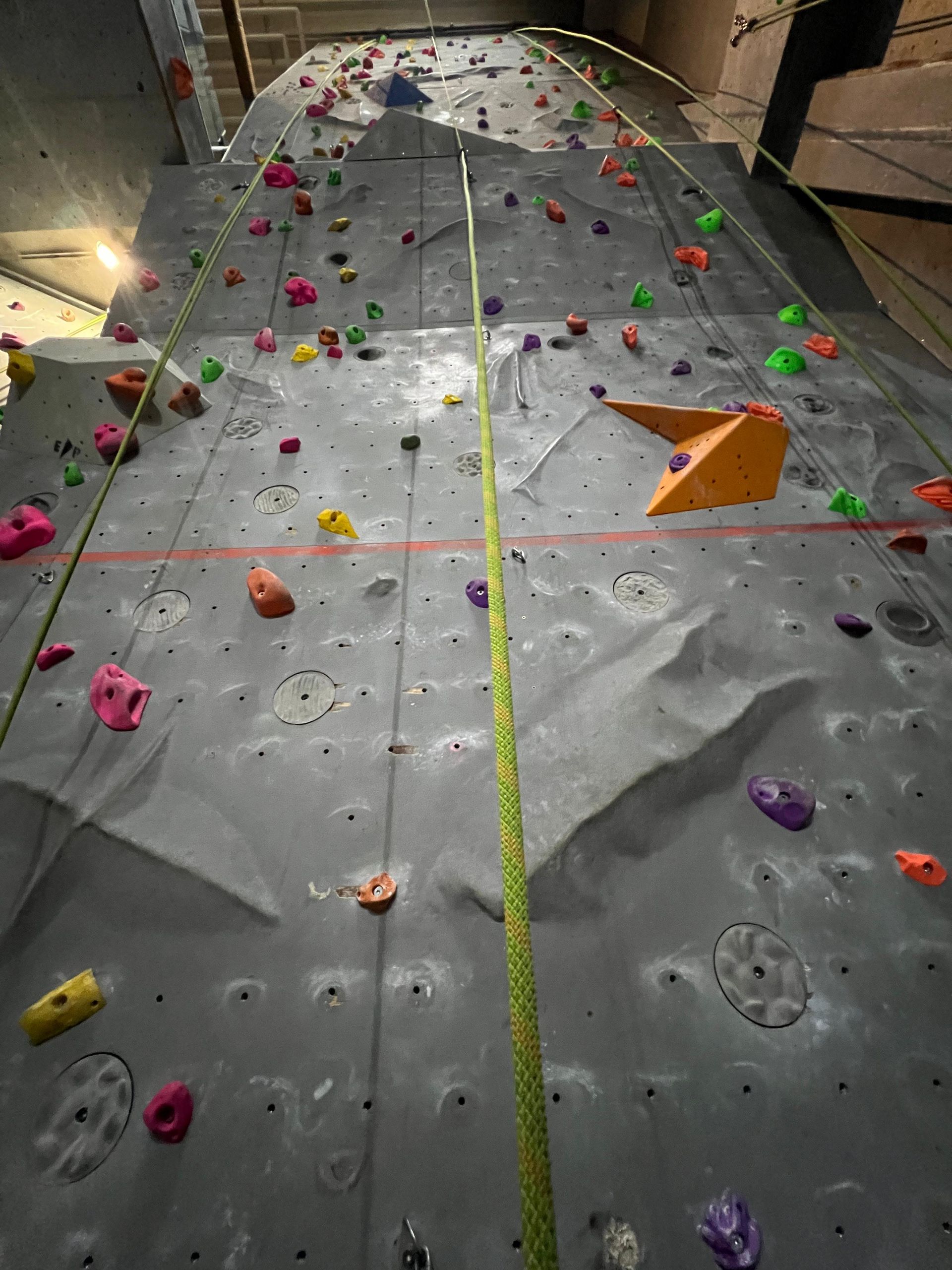 Kletterwand mit farbigen Griffen und einem Seil.