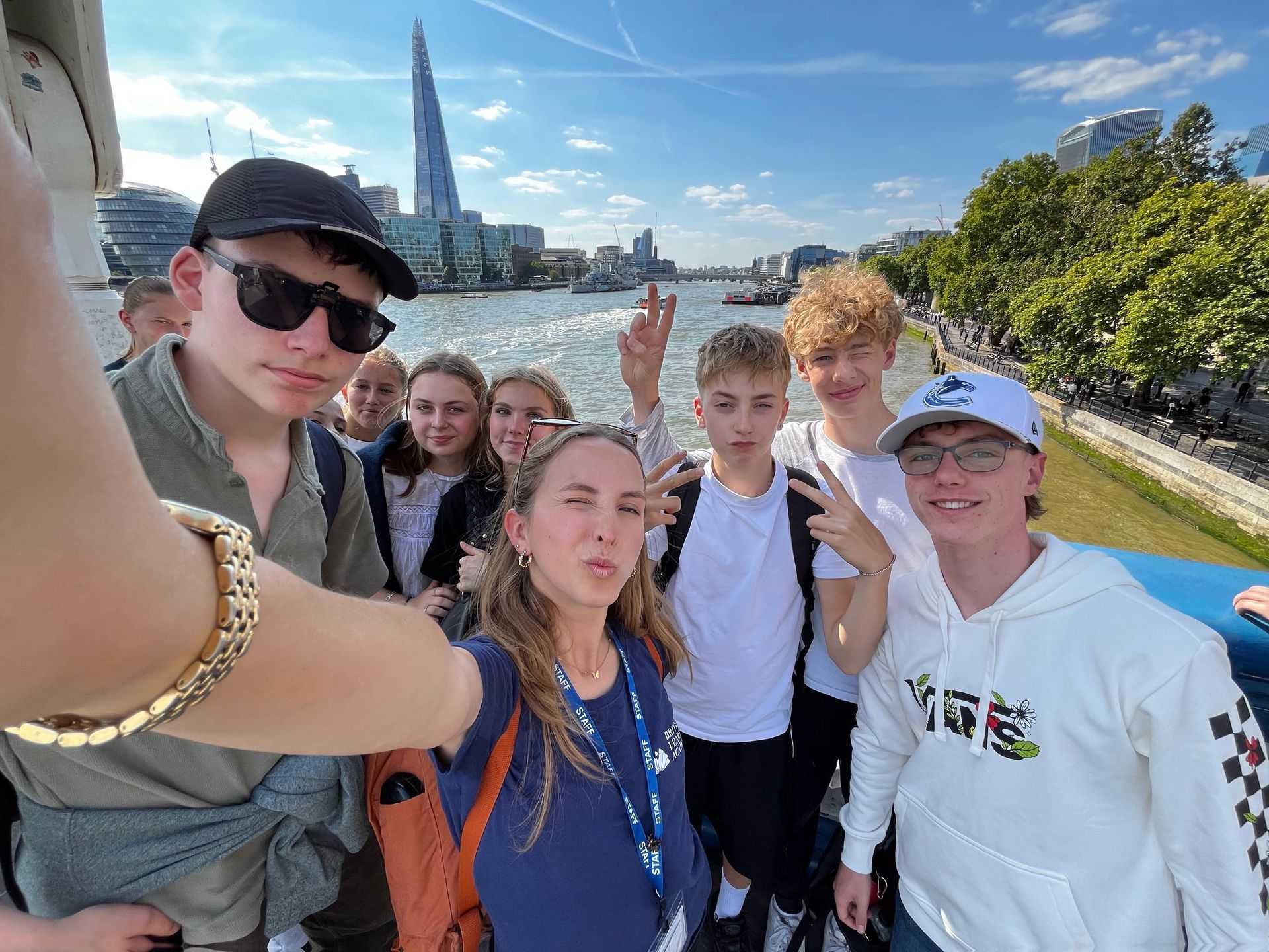 Eine Gruppe von Menschen macht ein Selfie auf einem Boot; im Hintergrund ist The Shard zu sehen. Sonniger Tag.