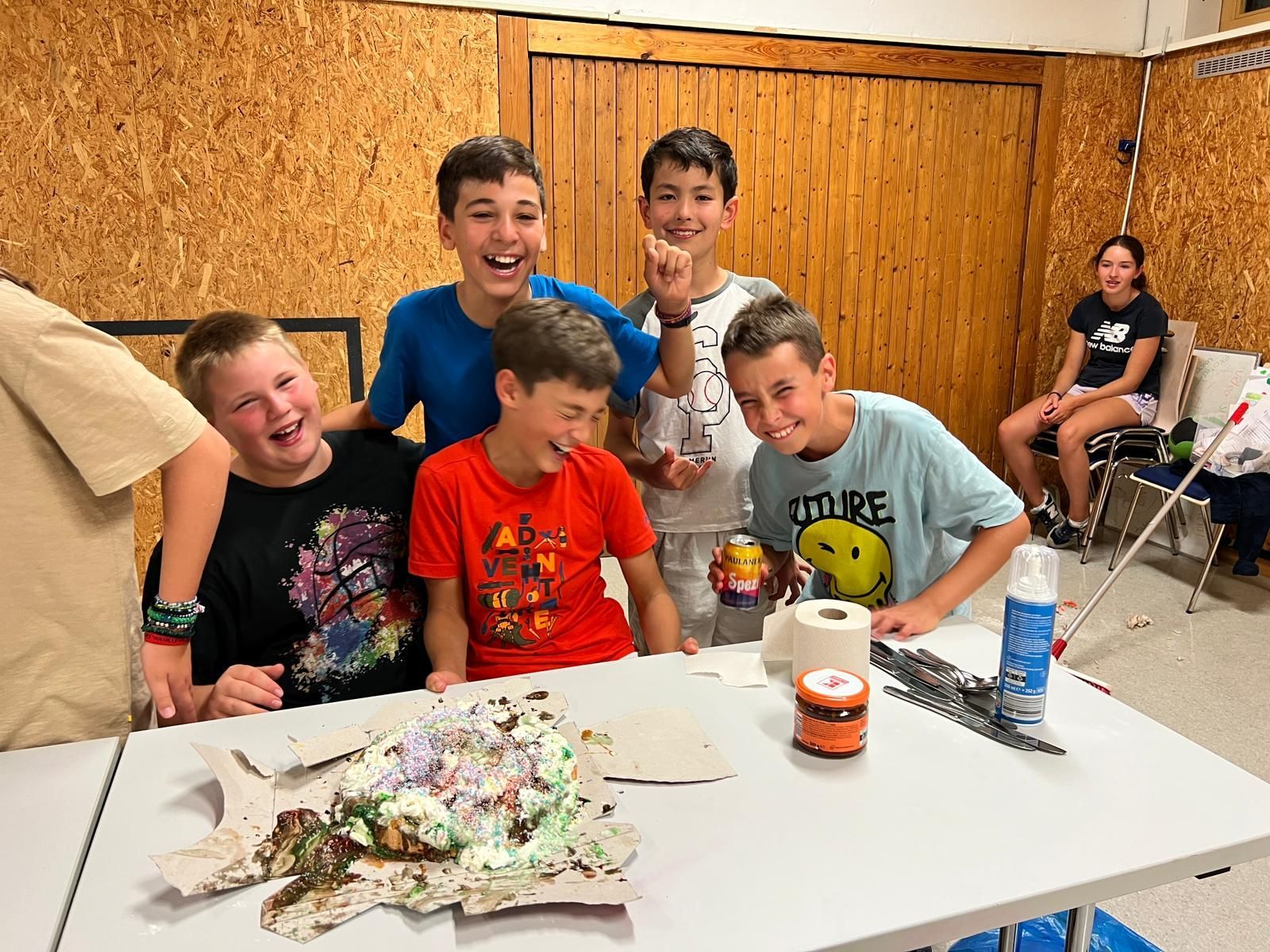Eine Gruppe kleiner Jungen sitzt mit einem Kuchen darauf um einen Tisch.