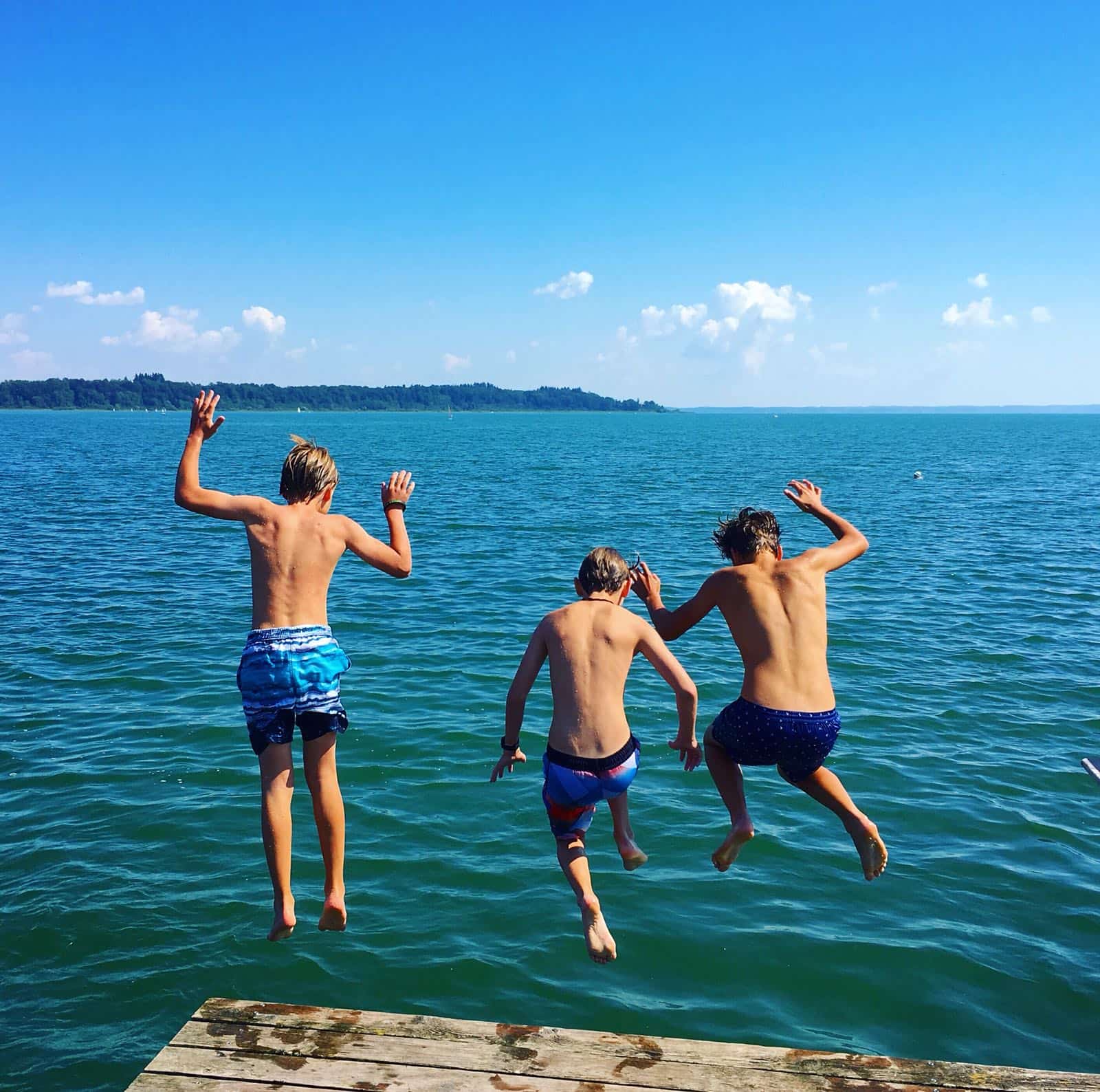 Drei Jungen springen von einem Steg ins Wasser