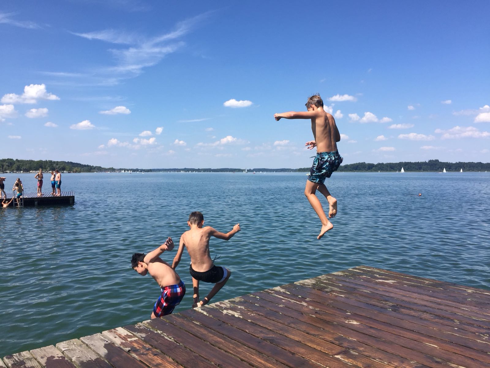 Drei Jungen springen von einem Steg in einen See.