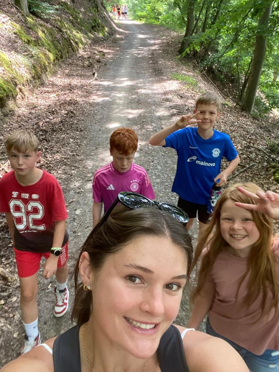 Eine Gruppe Kinder und eine Frau lächeln auf einem Feldweg in einem Waldgebiet in die Kamera.