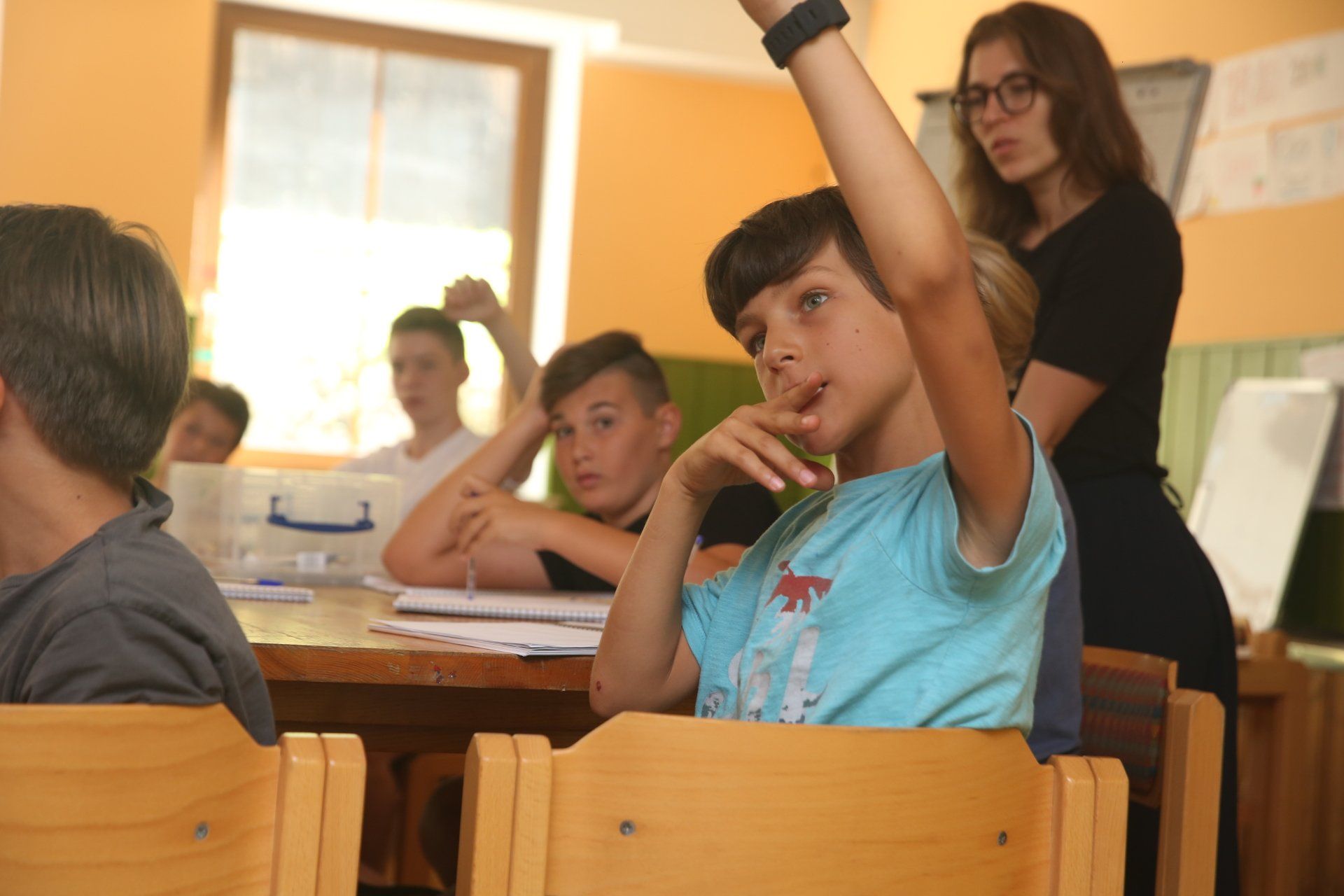 Ein Junge hebt in einem Klassenzimmer die Hand, um eine Frage zu beantworten