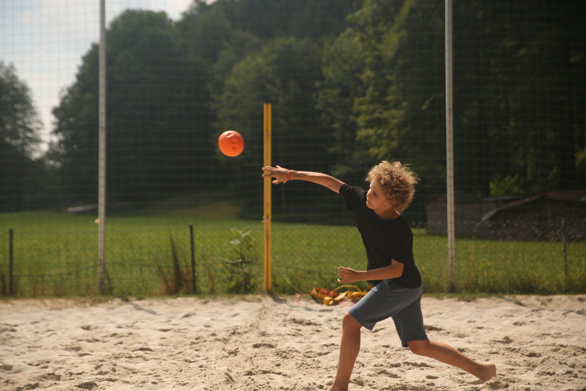 Ein kleiner Junge wirft einen orangefarbenen Ball in die Luft.