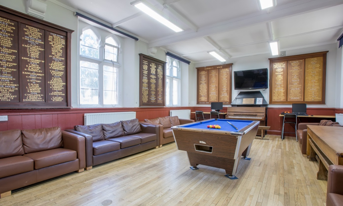 Ein Zimmer mit Billardtisch, Sofas und Klavier. Die Wände sind mit Holztafeln verziert, es gibt Fenster und einen Fernseher.