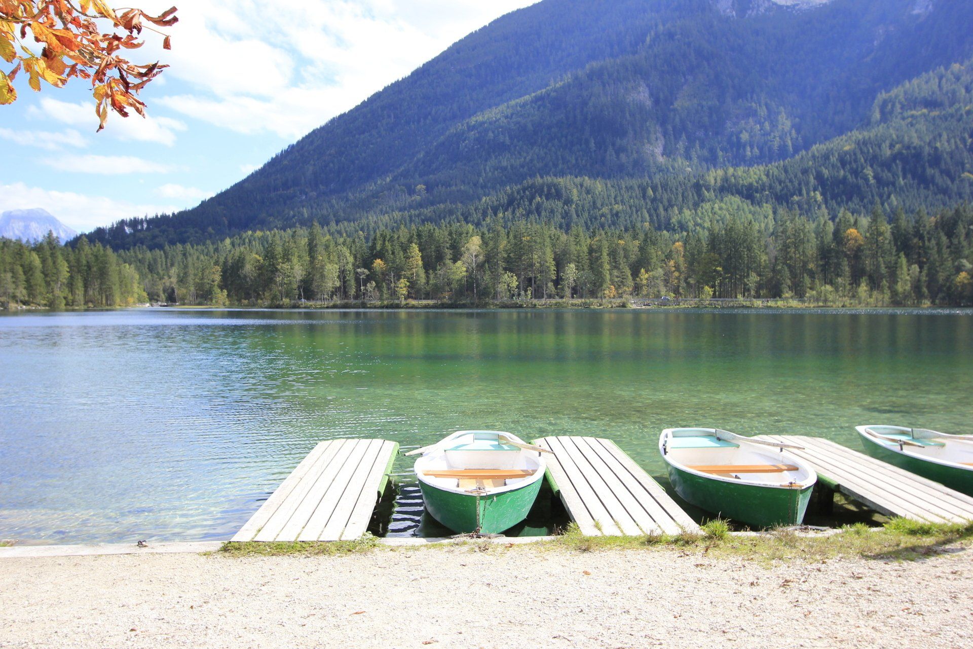 Grüne Ruderboote lagen an einem Holzsteg an einem klaren See vor einer Bergkulisse.