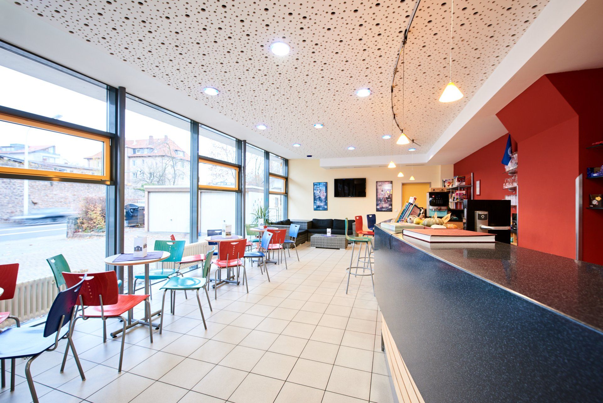 Café mit bunten Stühlen, großen Fenstern und einer Theke mit Kaffeemaschine.