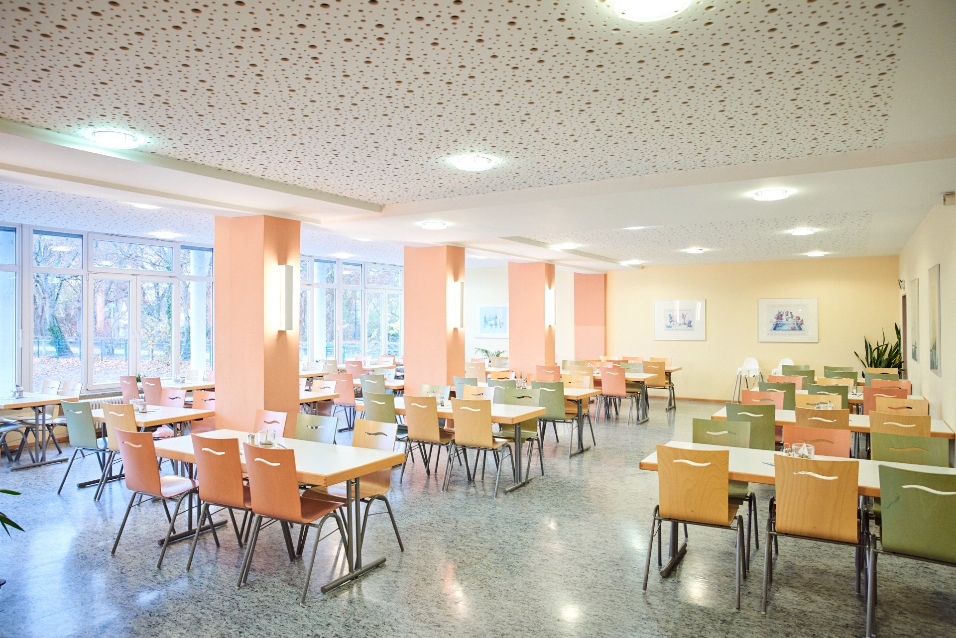 Speisesaal mit Tischen und Stühlen, beigen und grünen Akzenten, Terrazzoboden und gepunkteter Decke.