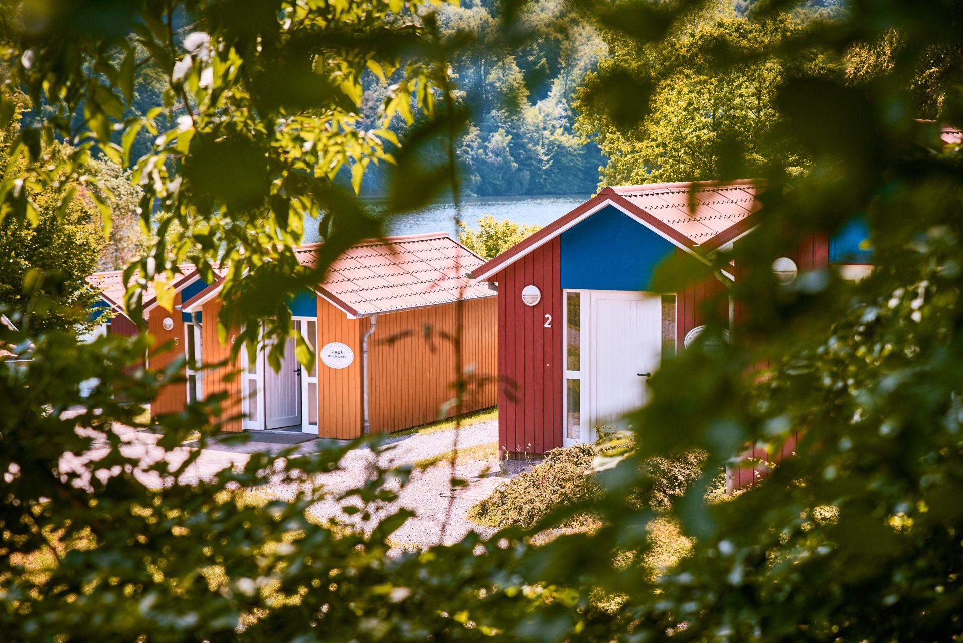 Bunte Hütten eingebettet in üppiges Grün, im Hintergrund ist ein See zu sehen.