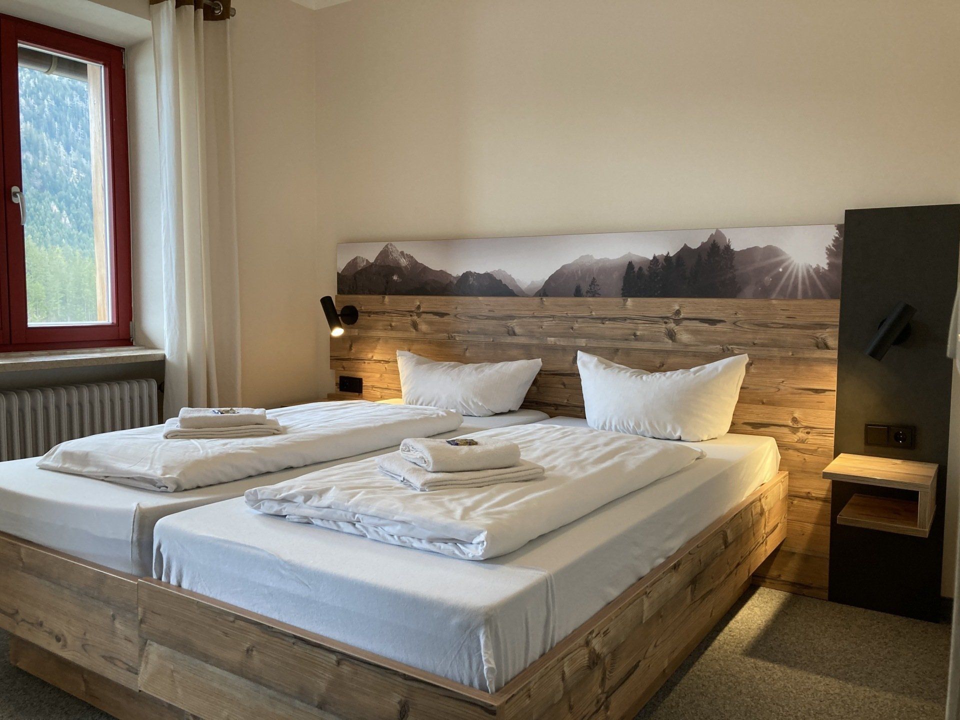 Zwei Einzelbetten in einem Hotelzimmer mit Bergmotiv am Kopfteil und Fenster.