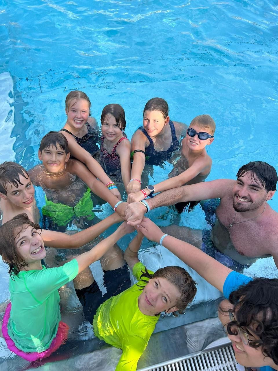 Eine Gruppe von Menschen in einem Pool, die Hände im Kreis gefaltet, lächelnd, feiernd.