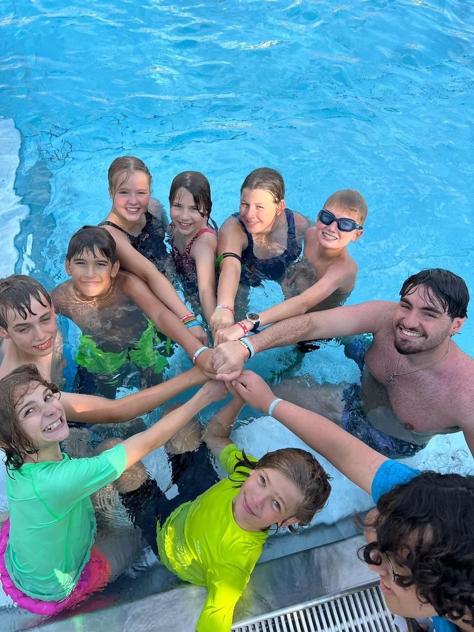 Eine Gruppe von Menschen in einem Pool, die Arme im Kreis gefaltet, lächelt in die Kamera.