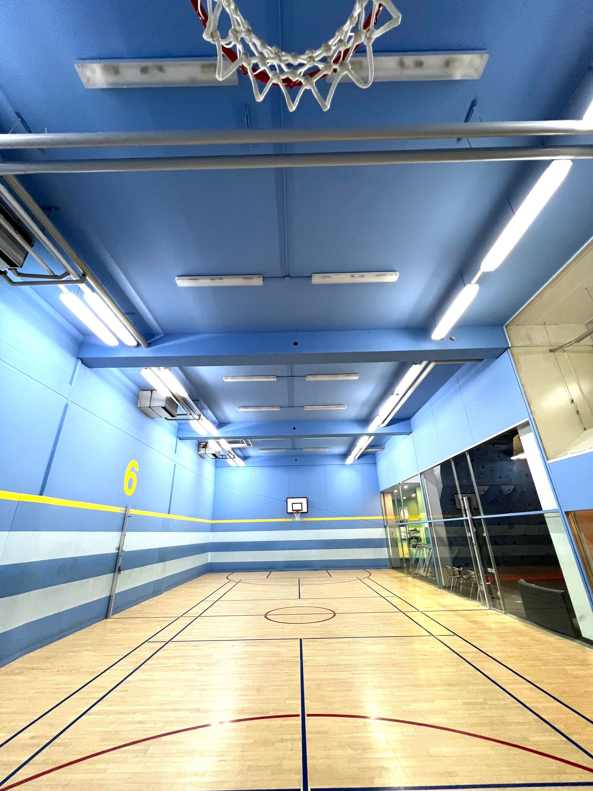 Indoor-Basketballfeld mit Holzboden, blauen Wänden und Körben.