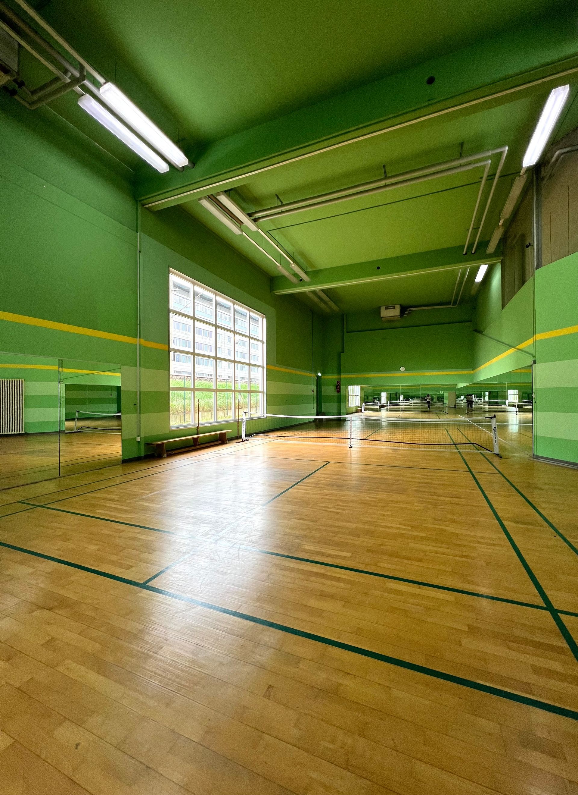 Turnhalle mit grünen Wänden, Holzboden, Spiegeln und großem Fenster.