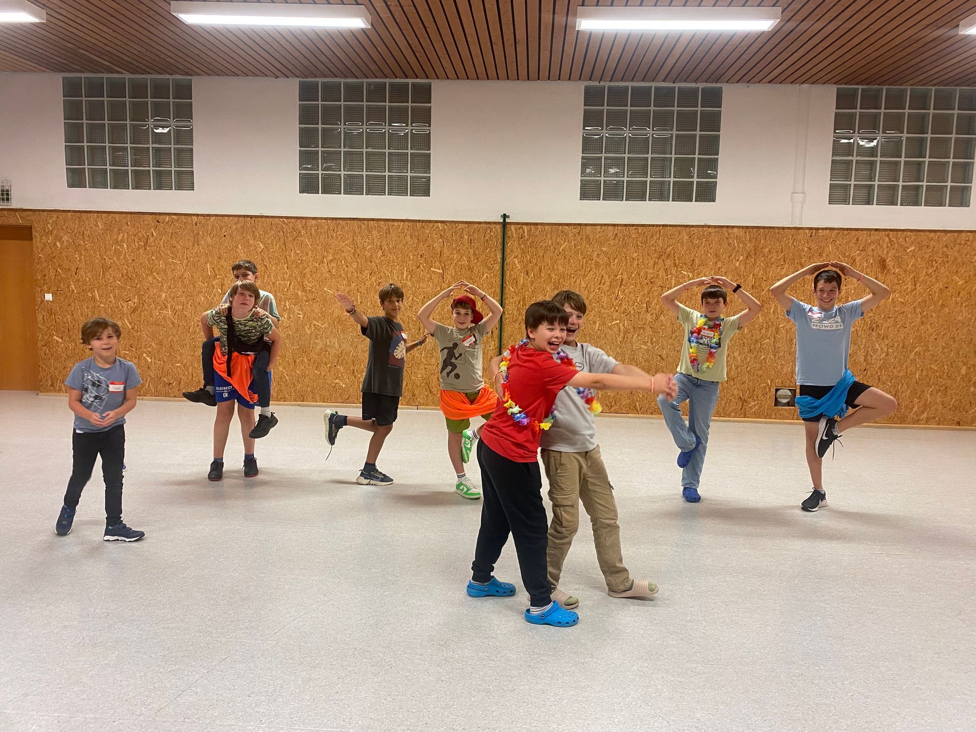 Kinder in einem Raum, einige tanzen, eines balanciert auf einem Bein. Neutraler Hintergrund.