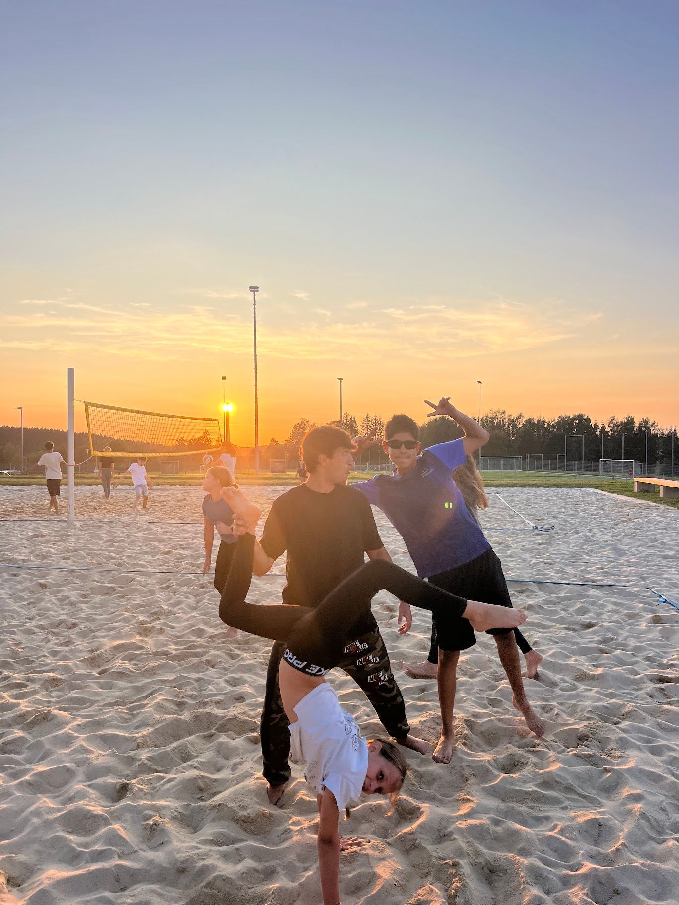 Menschen machen bei Sonnenuntergang Handstände am Strand. Zwei Männer schauen lächelnd zu.