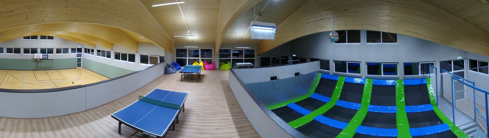 Indoor-Sporthalle mit Trampolinen, Sandkasten und Tischtennisplatte.