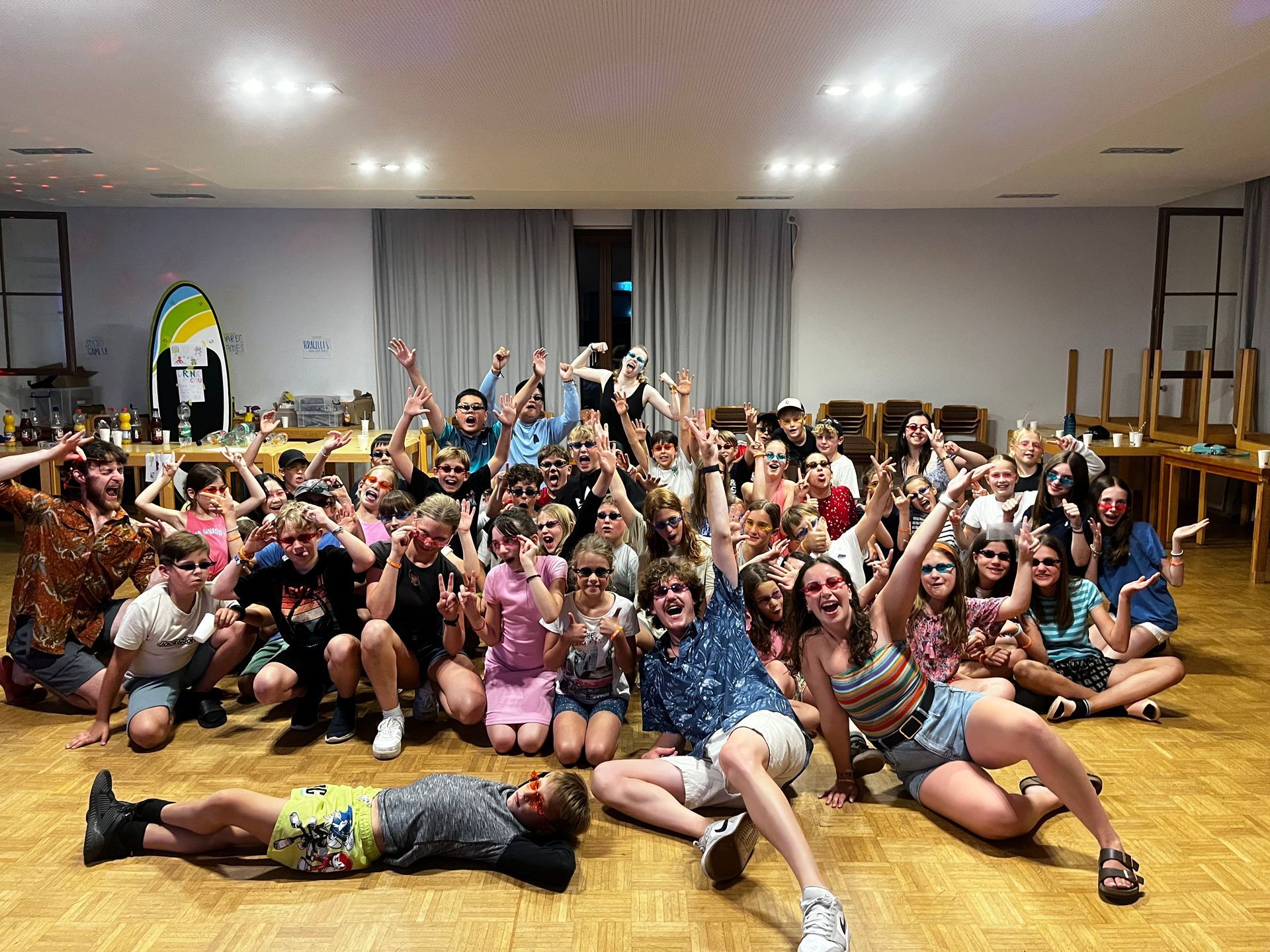 Eine große Gruppe von Menschen, hauptsächlich Kinder, jubelt begeistert in einem Raum; einige tragen Hawaiihemden.