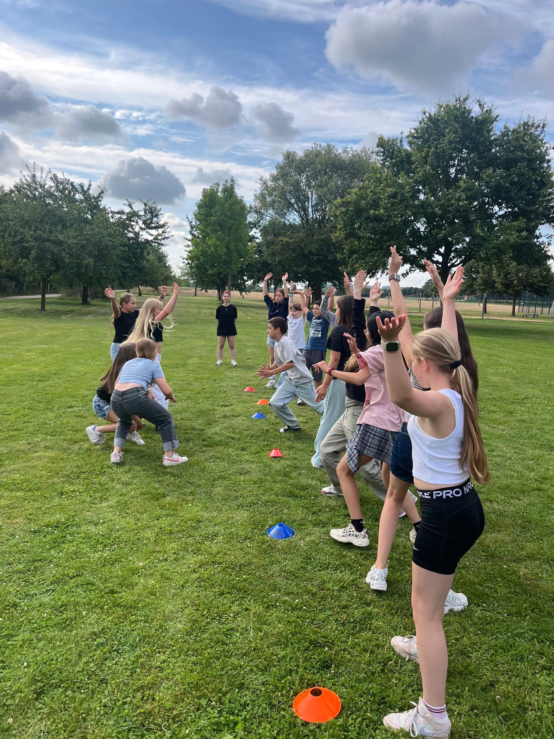 Eine Gruppe von Menschen spielt ein Spiel im Freien auf einer Rasenfläche; einige haben die Arme erhoben.