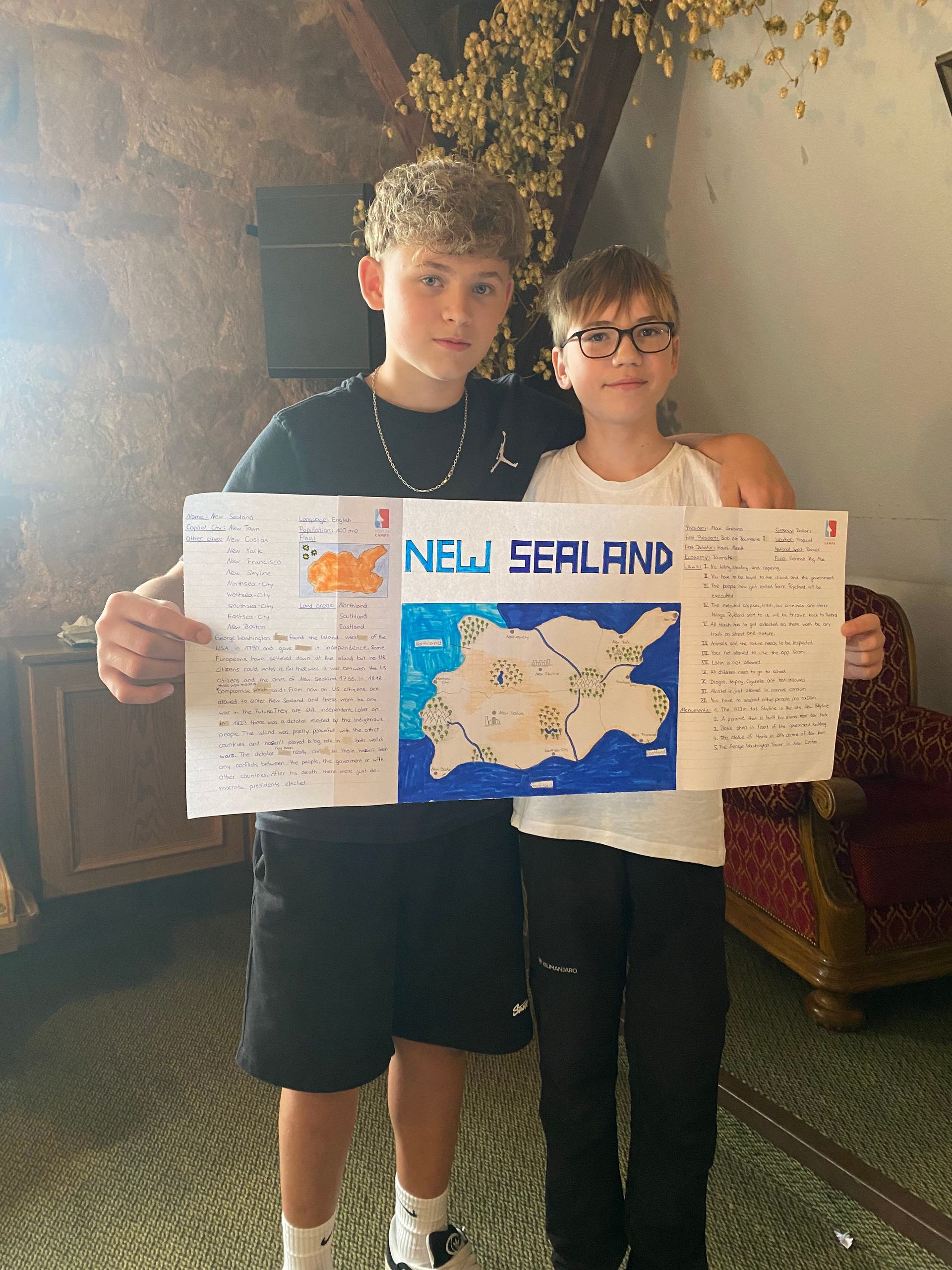 Zwei Jungen halten in einem Zimmer ein selbstgemachtes Poster über Neuseeland.