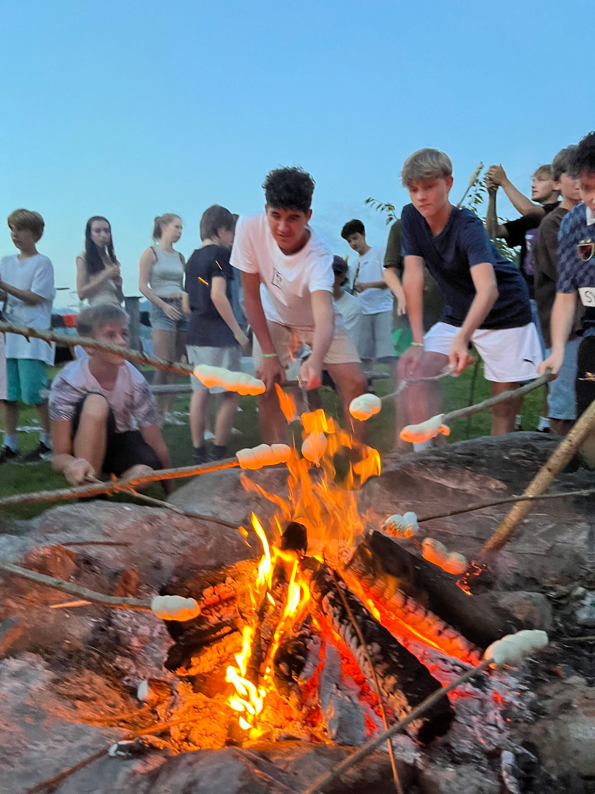 Menschen rösten in der Abenddämmerung Speisen über einem Lagerfeuer.