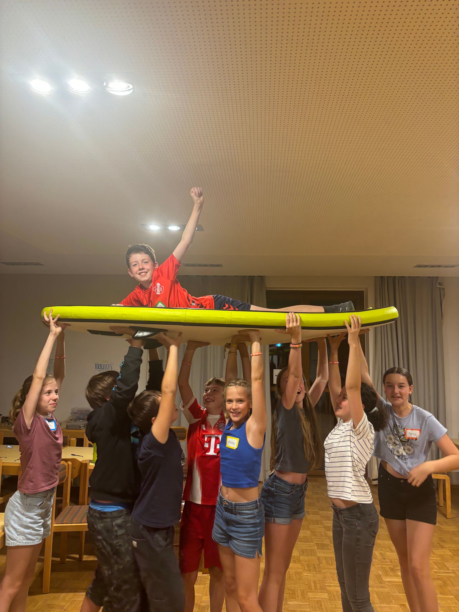 Eine Gruppe Kinder hält ein Schild mit einem Jungen darauf hoch und feiert.