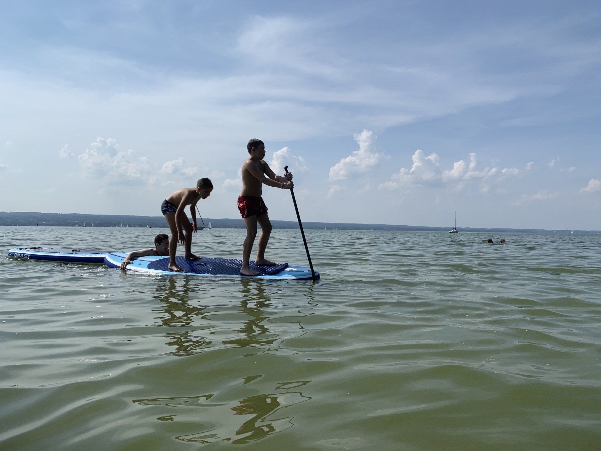 Ein Mann und zwei Kinder stehen auf einem Paddelbrett im Wasser.