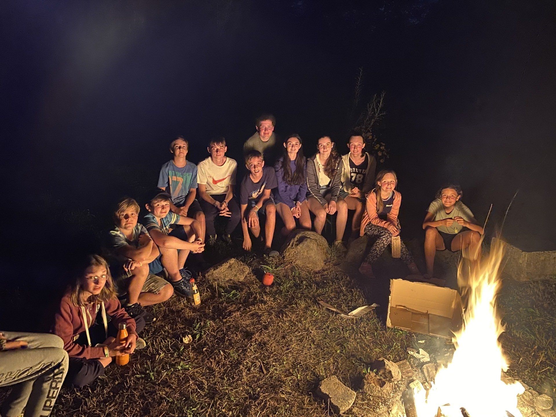 Eine Gruppe von Menschen sitzt nachts am Lagerfeuer.