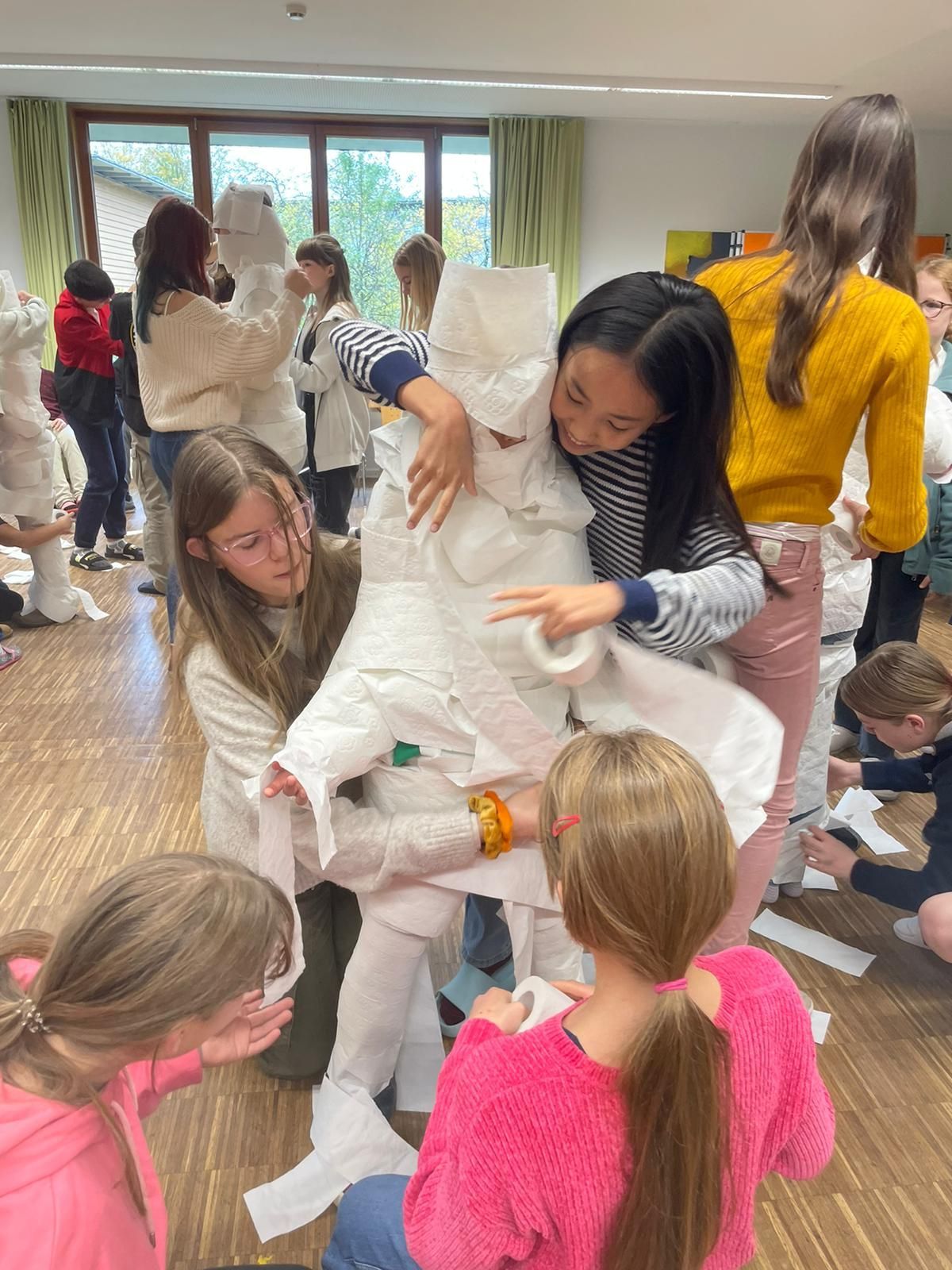 Eine Gruppe Kinder wickelt eine Mumie in Toilettenpapier ein.