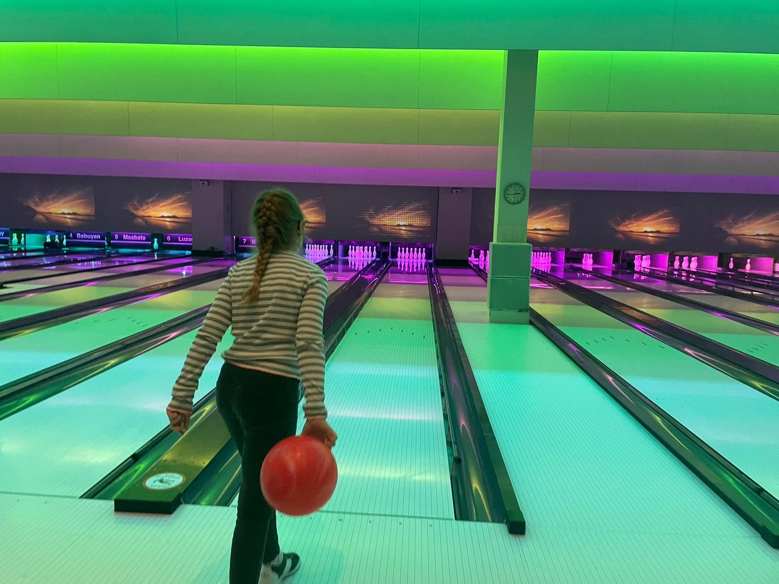 Ein junges Mädchen hält in einer Bowlingbahn eine Bowlingkugel.