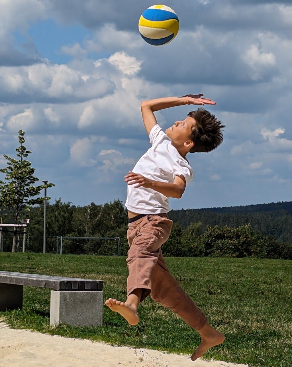 Ein Junge springt im Freien, um einen Volleyball zu schlagen. Der Ball ist gelb, blau und weiß.