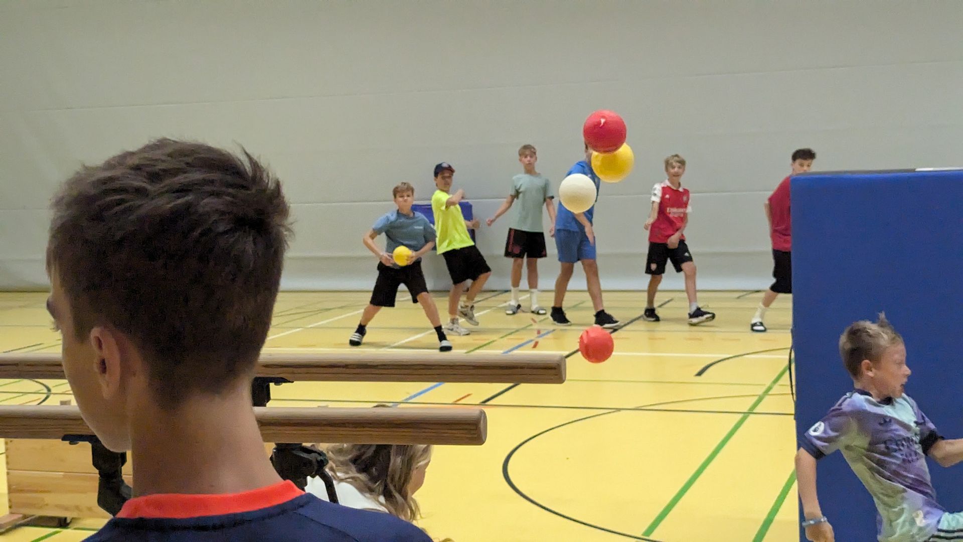 Kinder spielen Völkerball in einer Turnhalle; Bälle in der Luft.