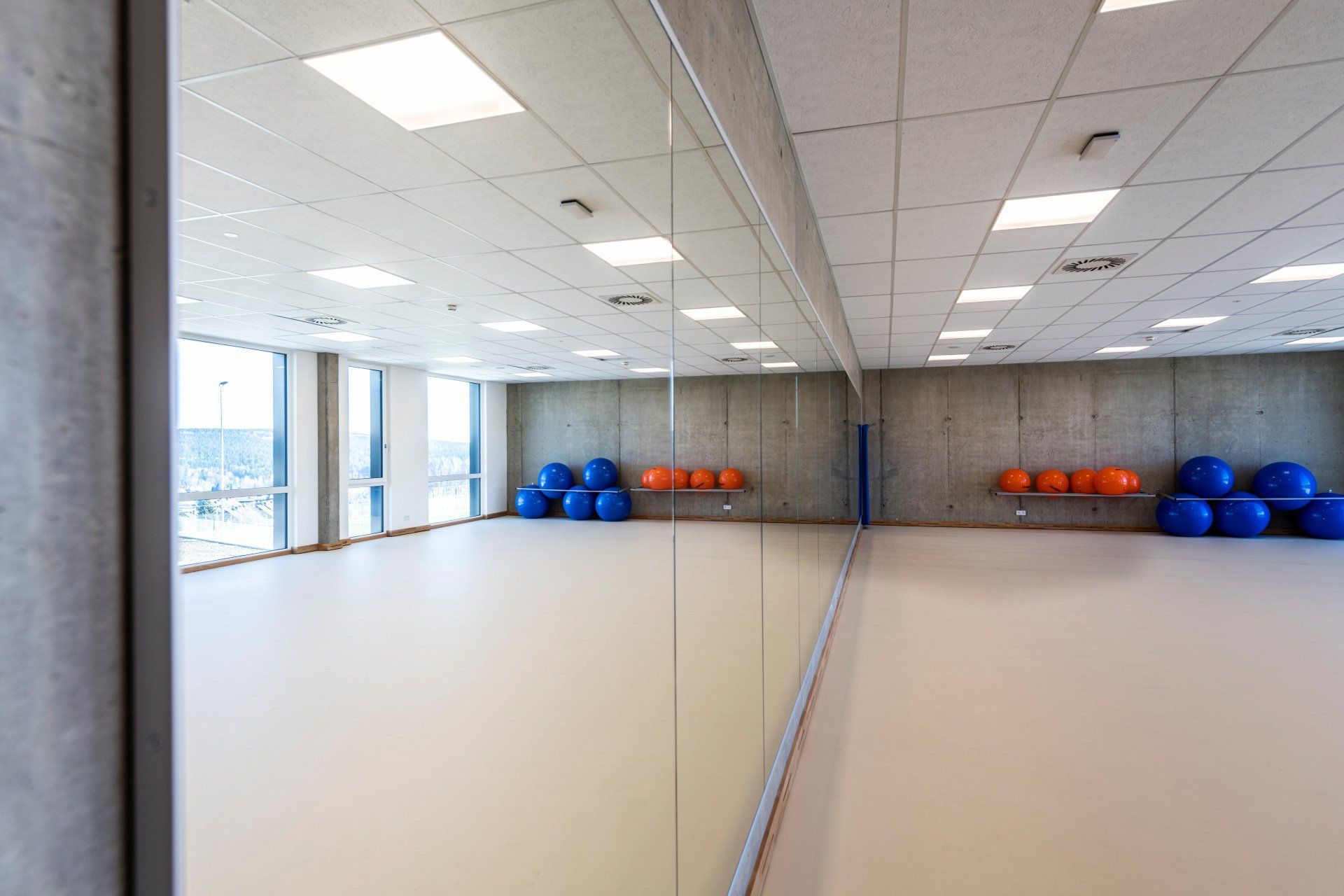Fitnessraum mit großem Spiegel, Gymnastikbällen und Fenstern.