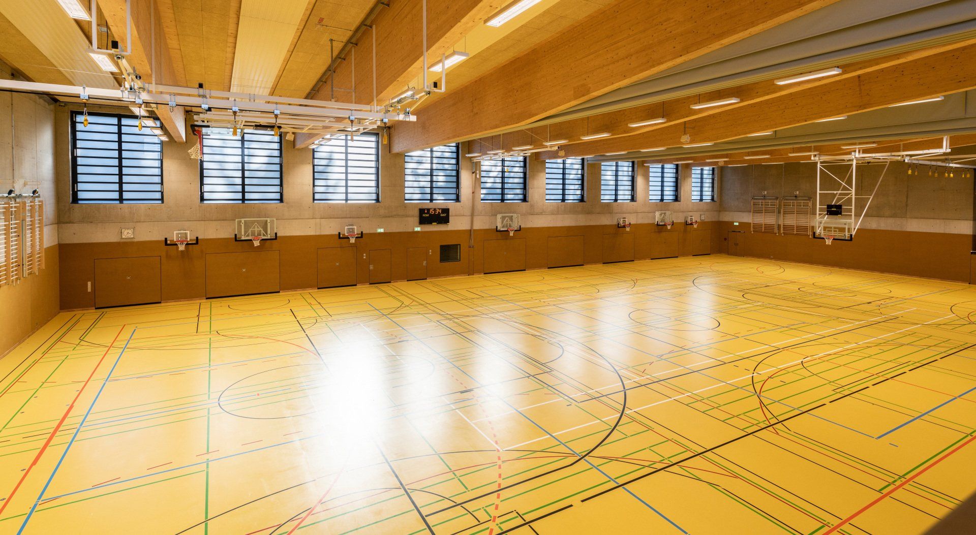 Leere Turnhalle mit Holzboden, Holzdecke und Holzwandpaneelen; Basketballkörben; Fenstern.