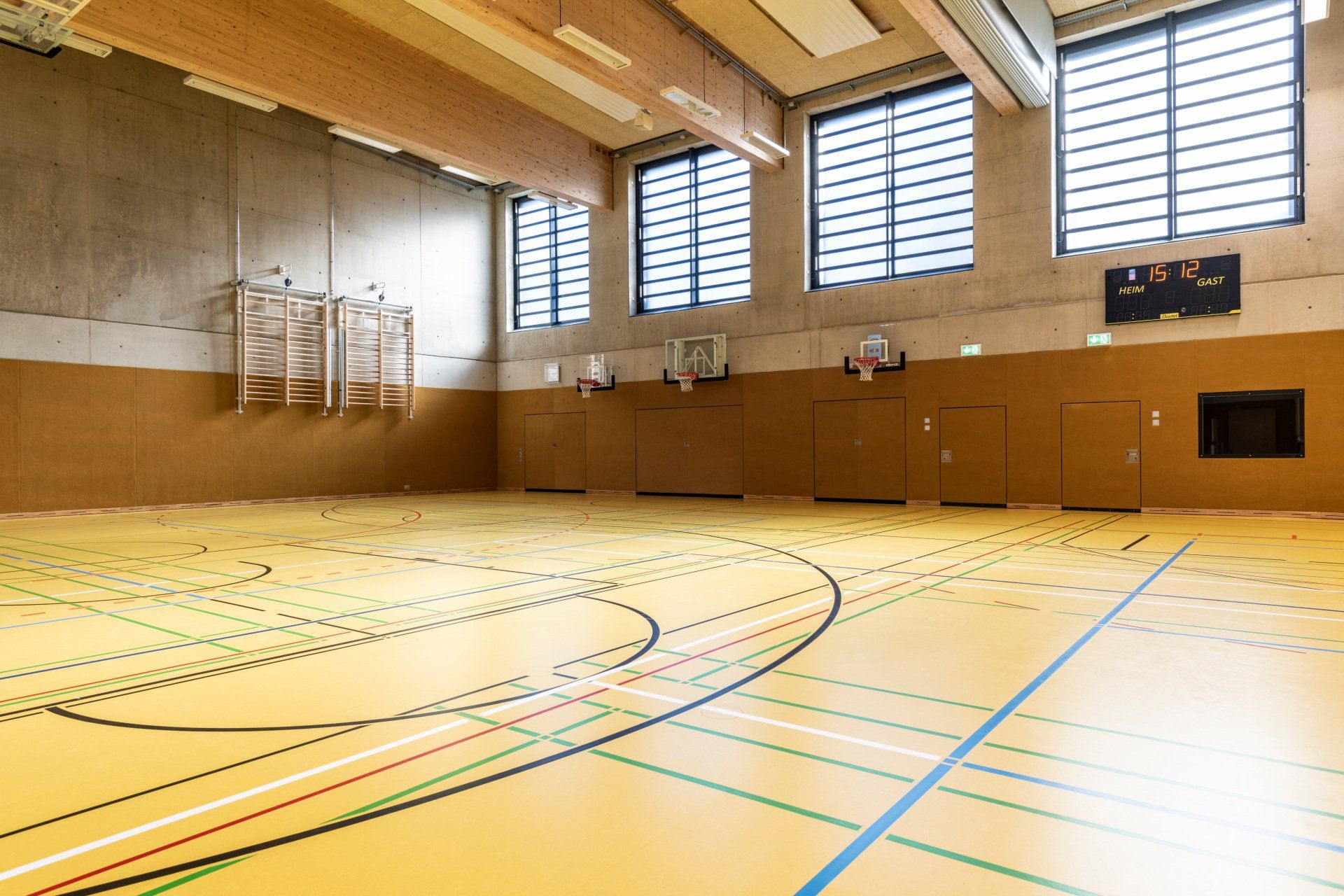 Turnhalle mit Holzboden, Basketballkörben und Fenstern.