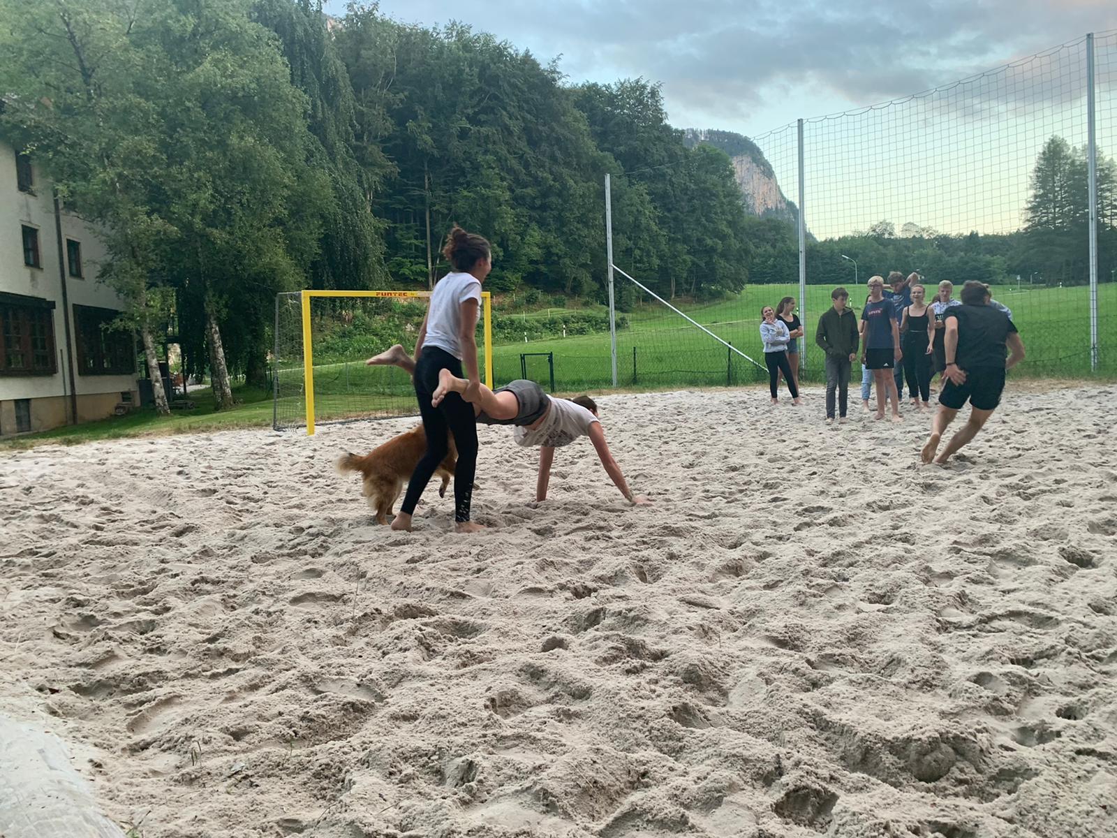 Eine Gruppe von Menschen spielt Volleyball auf einem Sandfeld.