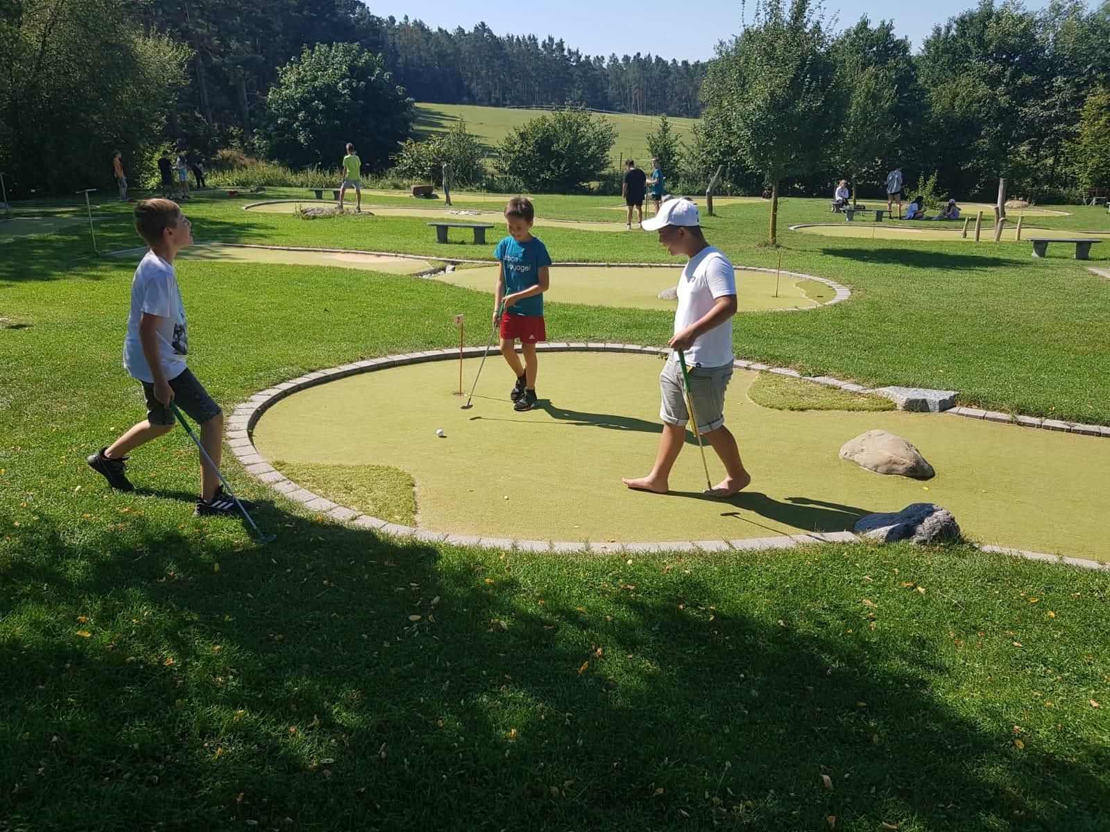 Drei Jungen spielen Minigolf an einem sonnigen Tag.