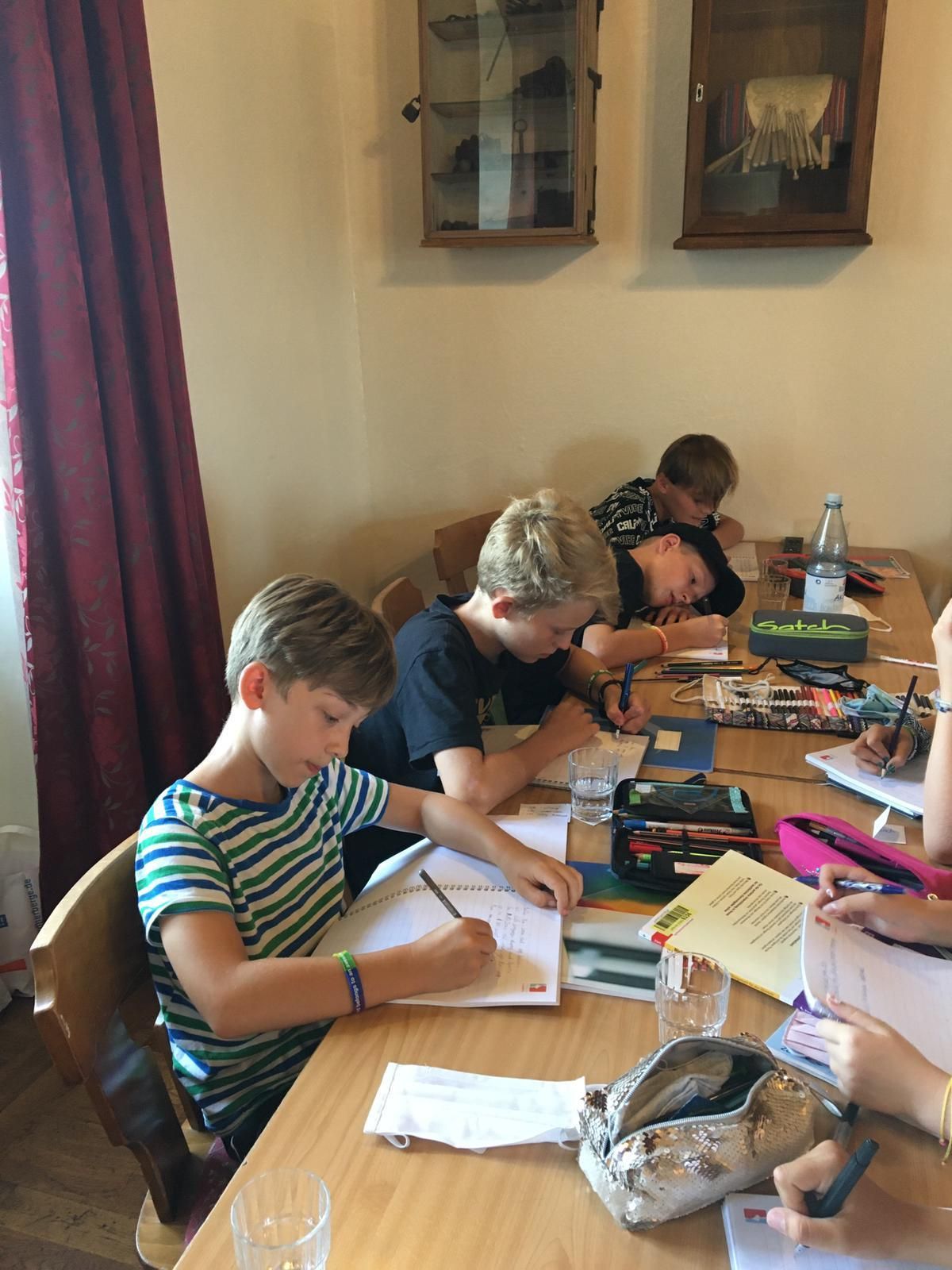 Kinder malen an einem Tisch in einem Zimmer. Ein Junge in einem gestreiften Hemd, andere zeichnen.