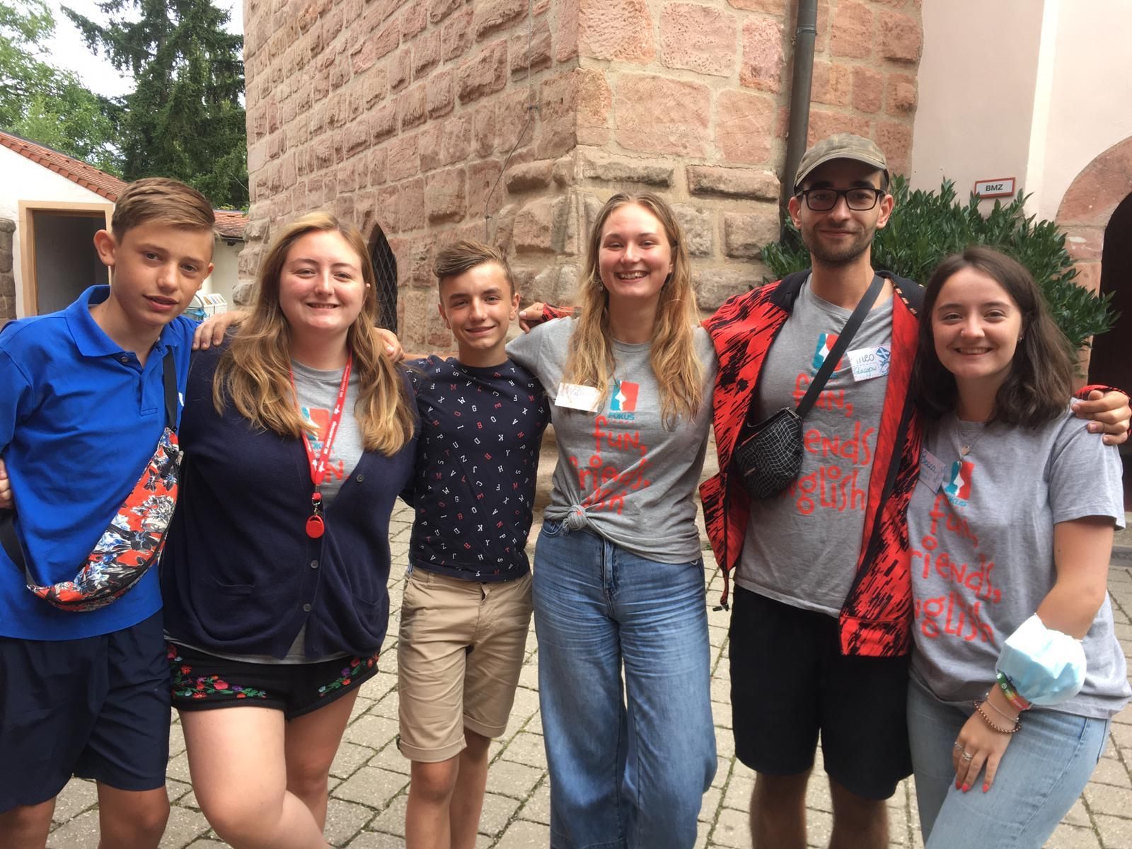 Eine Gruppe von Menschen posiert für ein Foto. Sie stehen vor einem Backsteingebäude. Einige tragen die gleichen T-Shirts.