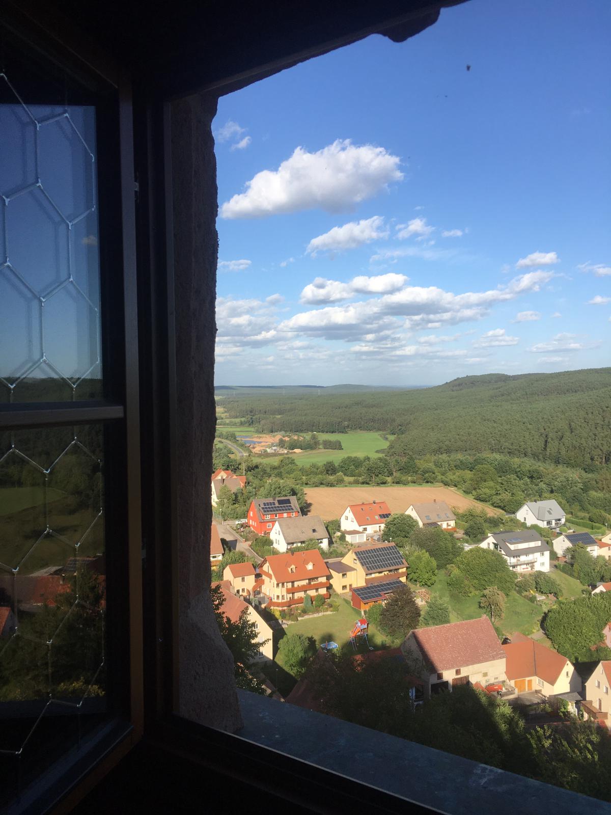 Ein Blick auf ein Dorf aus einem Fenster mit blauem Himmel und Wolken
