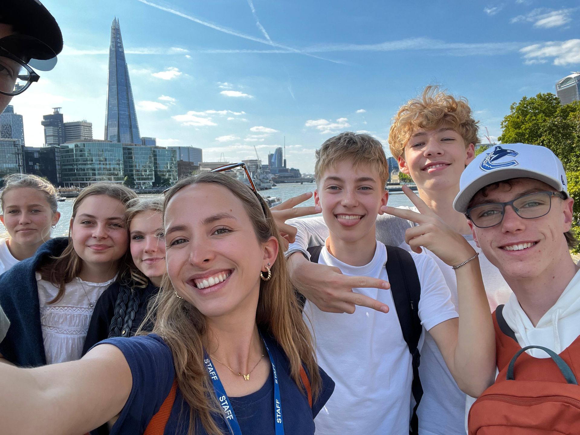 Eine Gruppe lächelnder Menschen macht ein Selfie vor der Londoner Skyline; sonniger Tag.